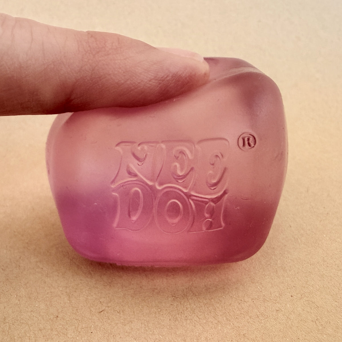 Finger pressing a pink NeeDoh Nice Ice Baby squish cube