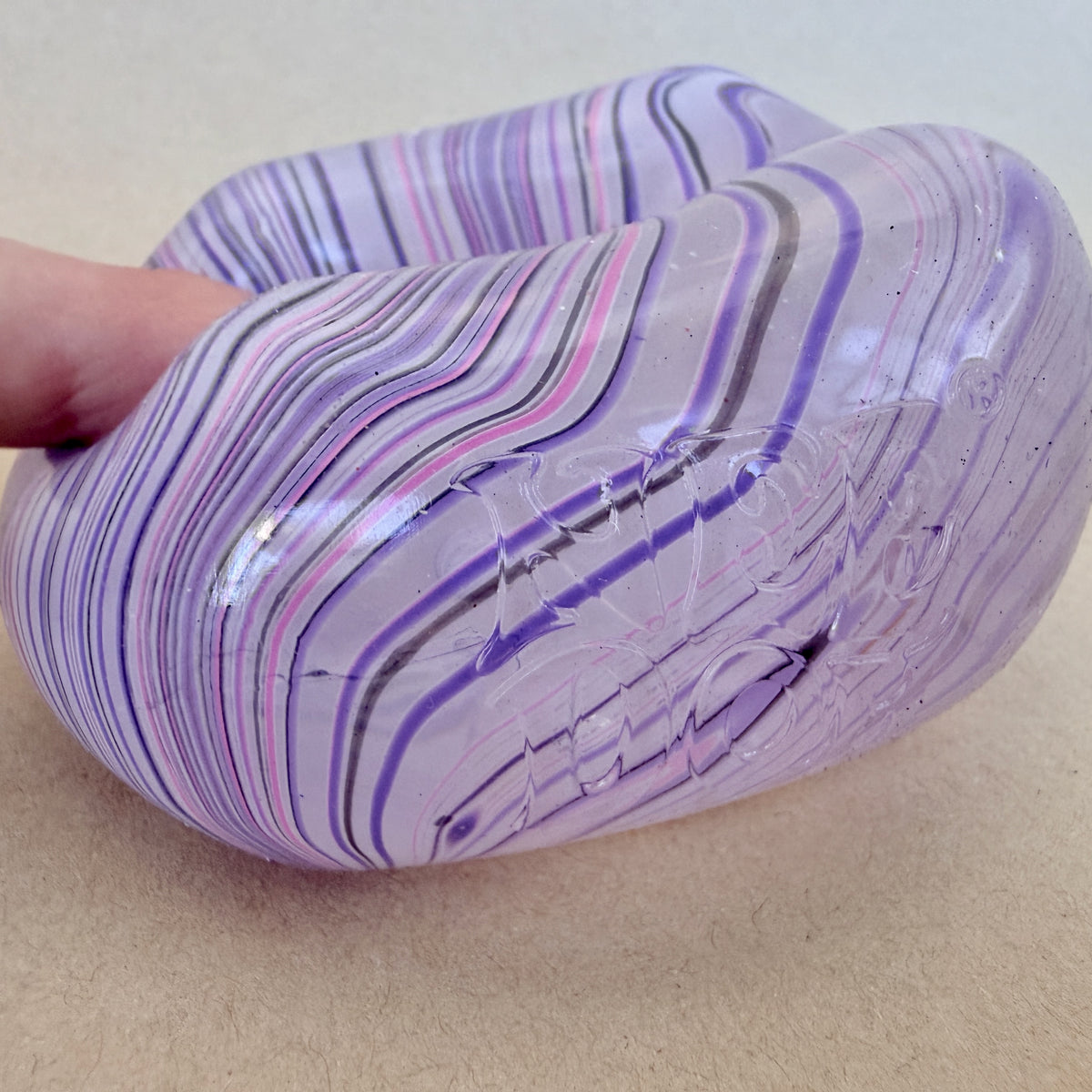 Hand squishing a marbled NeeDoh Nice Cube Swirl sensory toy