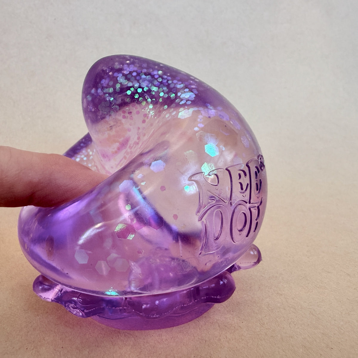 Hand squishing a glittery NeeDoh Dream Drop sensory toy